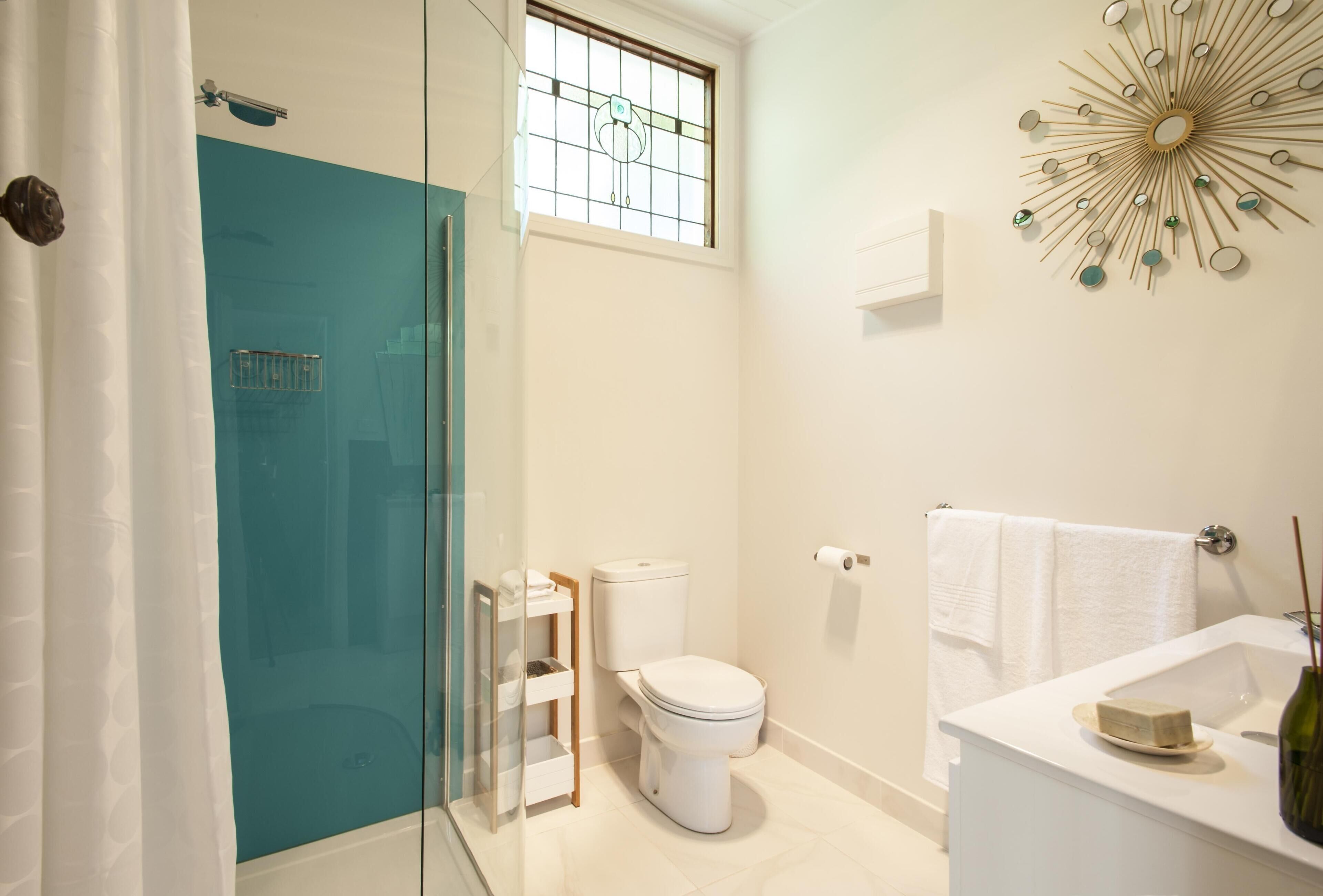 A bathroom with a glass shower enclosure, a toilet, a sink with a mirror, and a decorative wall piece.