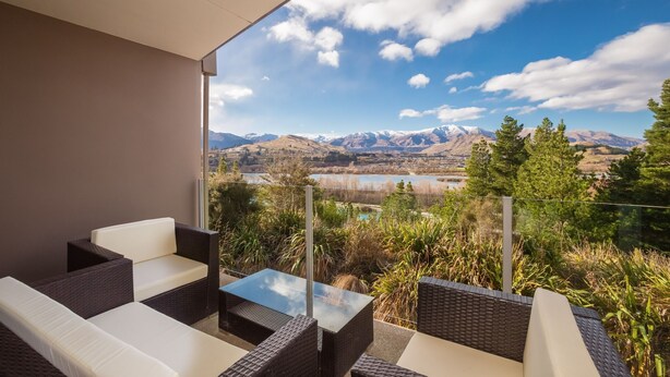 A balcony with wicker furniture and a glass table overlooking a mountainous landscape with a lake. - First in the Sun. Quiet 1st floor apartment. Fantastic River and Mountain Views (Frankton)