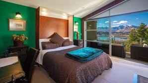 A bedroom with a large bed, green walls, and a view of mountains through a sliding glass door. - First in the Sun. Quiet 1st floor apartment. Fantastic River and Mountain Views (Frankton)