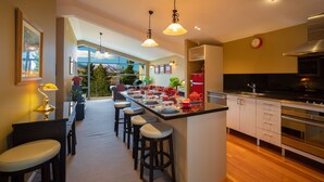 A modern kitchen with a central island, bar stools, and a view through the glass door. - First in the Sun. Quiet 1st floor apartment. Fantastic River and Mountain Views (Frankton)