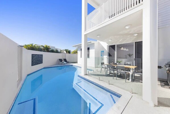 A modern house with a swimming pool, a balcony with outdoor furniture, and a clear view of the sky.