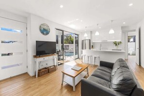 Una sala de estar moderna con un televisor de pantalla plana, un sofá, una mesa de centro y una cocina con taburetes de bar.