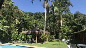 A pool area with lounge chairs and a thatched-roof structure. - Beach house with lots of greenery, a true beach country house.<br> 24-hour security. (Guarujá)
