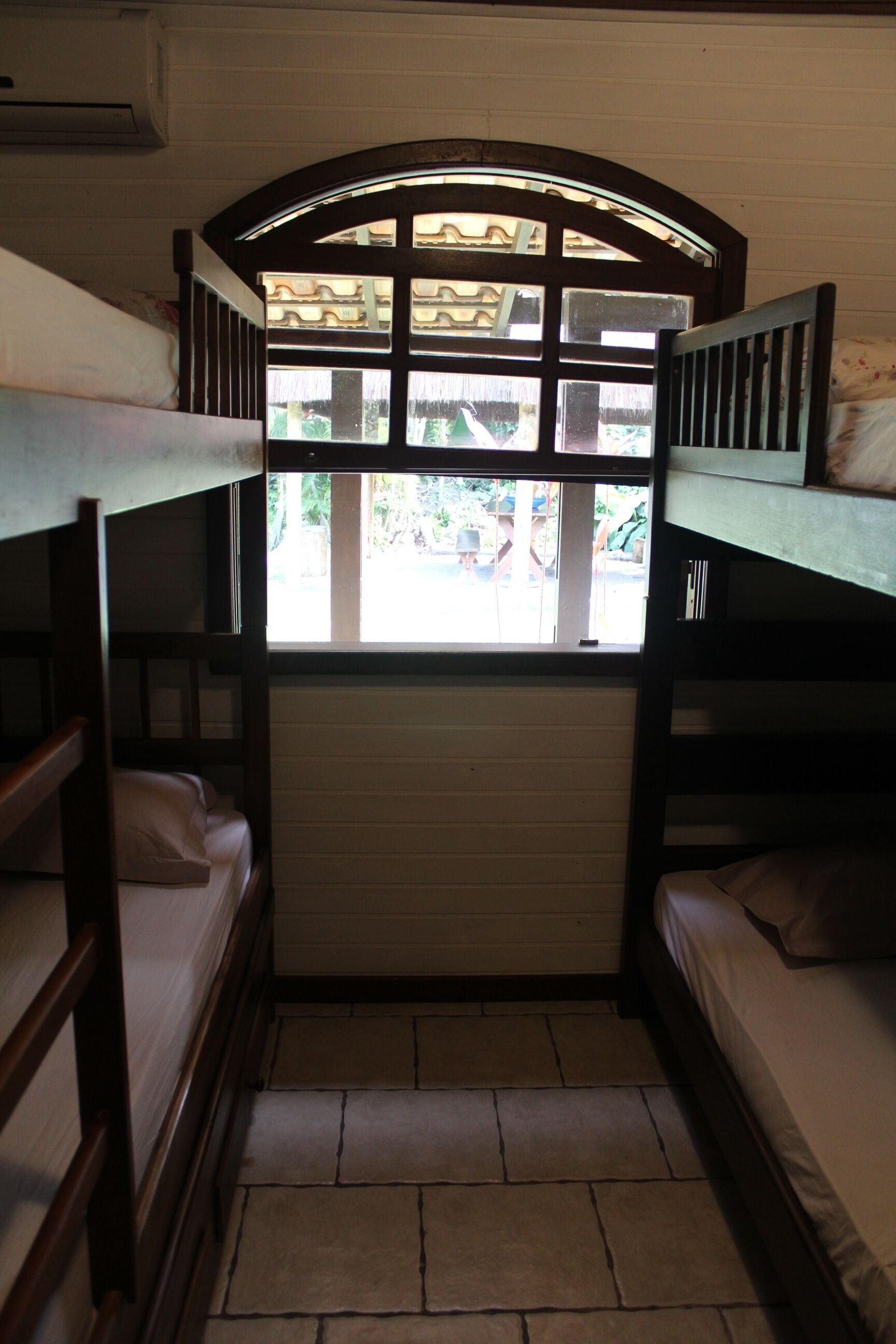 Una habitación estrecha con literas, una ventana de madera y una pared blanca.