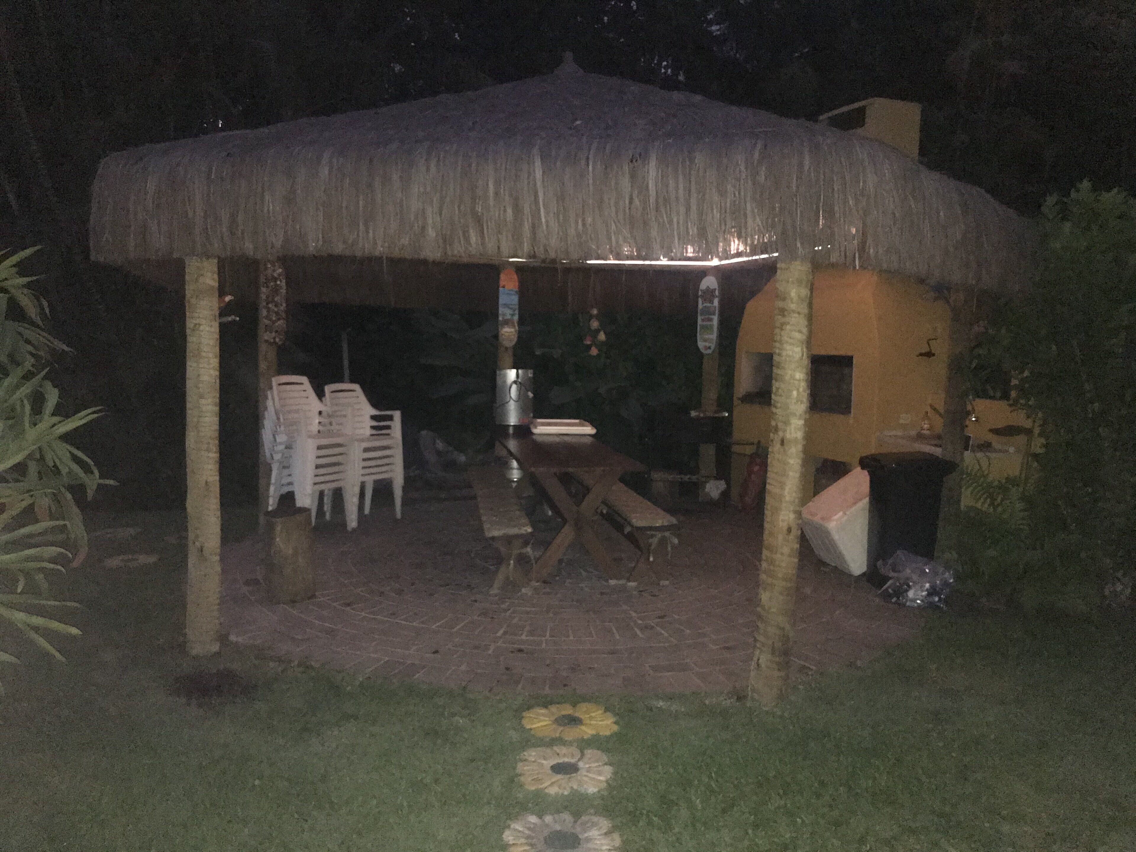 A covered outdoor area with a table and chairs, a trash bin, and a thatched roof structure.