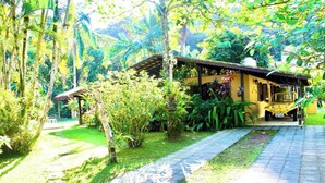 A rustic building with a thatched roof, surrounded by lush greenery and a paved pathway. - Beach house with lots of greenery, a true beach country house.<br> 24-hour security. (Guarujá)