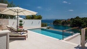 Zona de piscina con sillones de descanso, una planta en maceta y vista al mar.