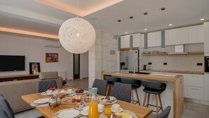 Un comedor moderno con una mesa de madera preparada para el desayuno, una lámpara colgante grande y una cocina al fondo.