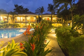 Ein Resort mit Schwimmbad, üppiger Bepflanzung und einem gut beleuchteten Gebäude mit mehreren Balkonen.