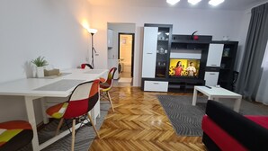 A modern living room with a dining area, a sofa, a TV, and a kitchen in the background. - Apartment Alina Deva (Deva)