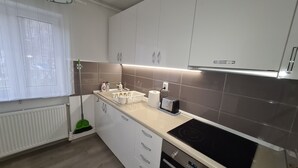 A modern kitchen with white cabinets, a built-in oven, a countertop with a toaster, and a window with blinds. - Apartment Alina Deva (Deva)