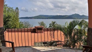 A balcony with a view of a lake and mountains, a tiled floor, and a stone wall. - Oceanview Studio Apartment w/ Community Pool & Views of Flamingo Marina (Playa Flamingo)