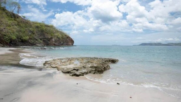 A beach with clear water, a rocky outcrop, and a distant mountain range. - Oceanview Studio Apartment w/ Community Pool & Views of Flamingo Marina (Playa Flamingo)