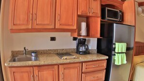 A compact kitchen with wooden cabinets, a stainless steel refrigerator, a microwave, and a coffee maker. - Oceanview Studio Apartment w/ Community Pool & Views of Flamingo Marina (Playa Flamingo)