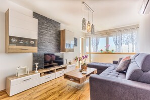 A modern living room with a flat-screen TV, wooden and white furniture, a stone accent wall, and a large window with curtains. - Cozy sea view apt. with heated pool and football court (Kaštel Stari)