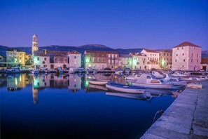 A marina with boats docked, a tower, and buildings with illuminated windows. - Cozy sea view apt. with heated pool and football court (Kaštel Stari)