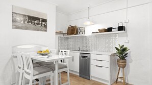 Een moderne keuken met witte kastjes, een ingebouwde vaatwasser en een eethoek met een witte tafel en stoelen.