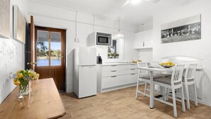 Een moderne keuken met witte kastjes, een houten eettafel en een uitzicht door de deur.