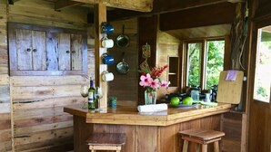 A rustic wooden kitchen with a bar area, wooden stools, and a window with a view of greenery. - Dragon fly Cottage (Cave)