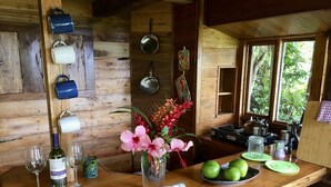 A wooden cabin kitchen with a wooden counter, hanging pots, a stove, and a window with a view of greenery. - Dragon fly Cottage (Cave)
