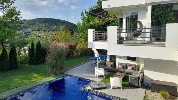A modern two-story house with a swimming pool, outdoor seating, and a view of a green landscape. - PRIVATE Family VILLA with jakuzzi & swimming pool (Budaörs)
