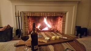 A fireplace with a burning log, a bottle of wine, a glass of wine, and some cheese and crackers on a wooden board. - Lake House Benalla-  Late Sunday checkout available upon request (Benalla)