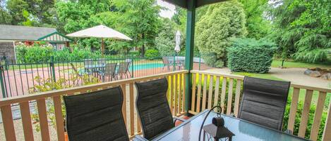 A covered outdoor seating area with a glass table and chairs, surrounded by a metal fence and greenery.