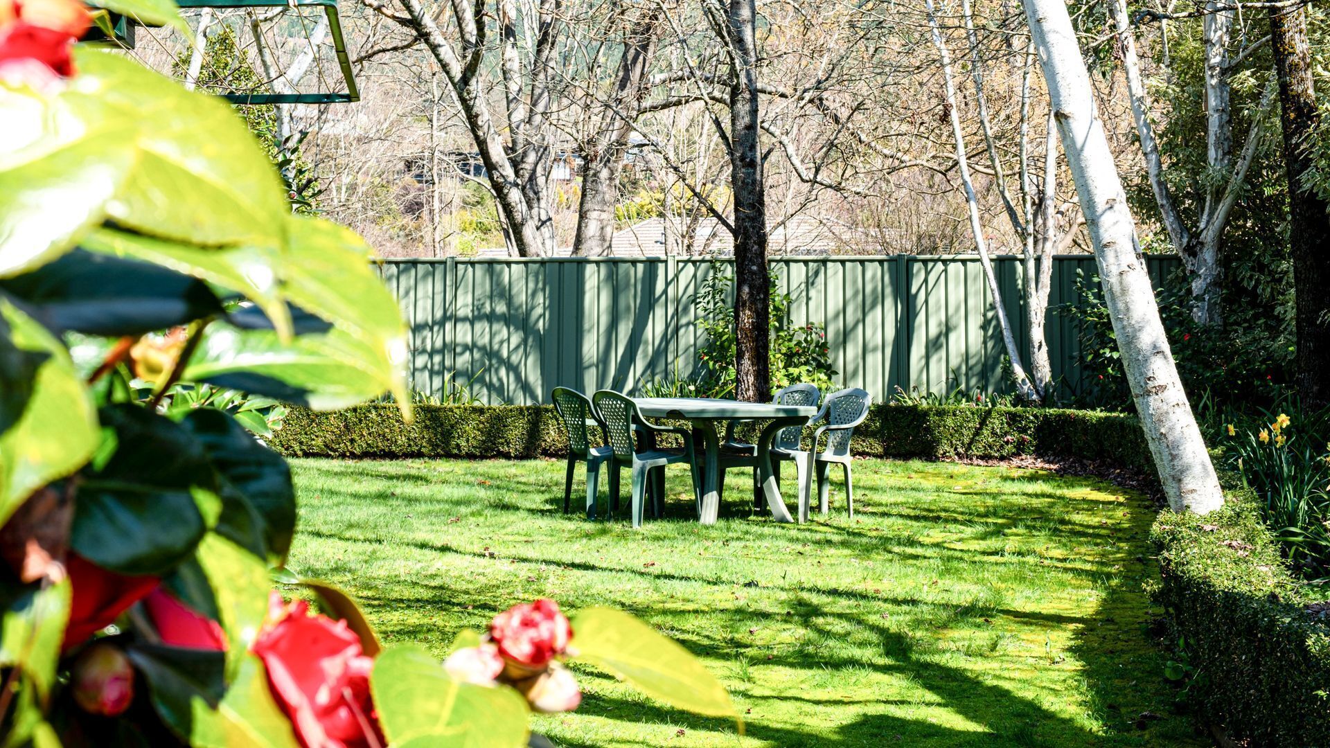 Un jardin bien entretenu, agrémenté d’une table et de chaises pour les repas, entouré d’une végétation luxuriante et délimité par une clôture en bois.