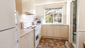Une cuisine compacte avec des meubles blancs, une cuisinière, un four à micro-ondes et une fenêtre donnant sur un jardin.