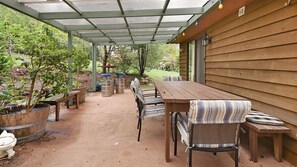 Eine Terrassensitzgruppe draußen mit Holztisch und Stühlen, umgeben von Topfpflanzen und einem überdachten Bereich mit Metallveranda.