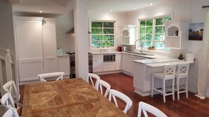 Una cocina moderna con armarios blancos, una mesa de comedor de madera y vistas al exterior con vegetación.