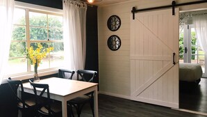 Un comedor con una mesa y sillas, una ventana con cortinas y una puerta corredera de estilo rústico.