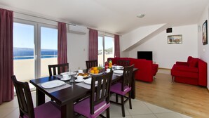 A dining area with a table set for four, a red sofa, and a balcony with a view of the sea. - Panoramic view, swimming pool, 9 bedrooms, fitness,  7 bathrooms, 16 persons (Omiš)