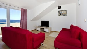 A modern living room with a large window, a flat-screen TV, and red sofas. - Panoramic view, swimming pool, 9 bedrooms, fitness,  7 bathrooms, 16 persons (Omiš)
