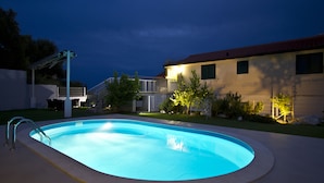 A swimming pool with a metal ladder, surrounded by a well-maintained lawn and a house with a red roof. - Panoramic view, swimming pool, 9 bedrooms, fitness,  7 bathrooms, 16 persons (Omiš)