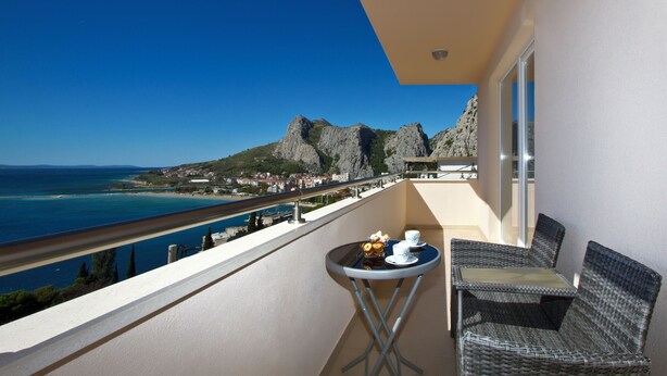 A balcony with a table and chairs, overlooking a coastal view with rocky cliffs and a beach. - Panoramic view, swimming pool, 9 bedrooms, fitness,  7 bathrooms, 16 persons (Omiš)