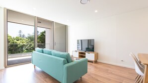 Ett modernt vardagsrum med en turkosfärgad soffa, en platt-TV på ett träställ och en matplats med ett träbord och stolar.