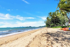 Une plage avec un ciel dégagé, des palmiers et une chaîne de montagnes qui se dessine à l’horizon.