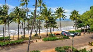 Une vue sur la plage, avec des palmiers, une route, des véhicules garés et un autobus.