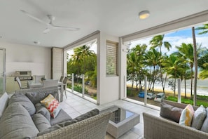 Un salon moderne avec un canapé, des fauteuils, une table basse et une vue sur la plage et les palmiers.