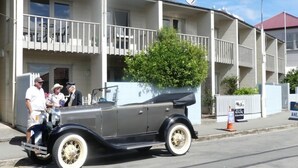 Ein altes Auto parkt vor einem Wohngebäude mit Balkonen und einem kleinen Baum.