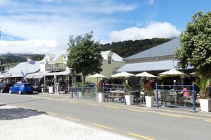A street with outdoor seating, a flag, and buildings with a hilly background. - Akaroa Central apartment (Akaroa)