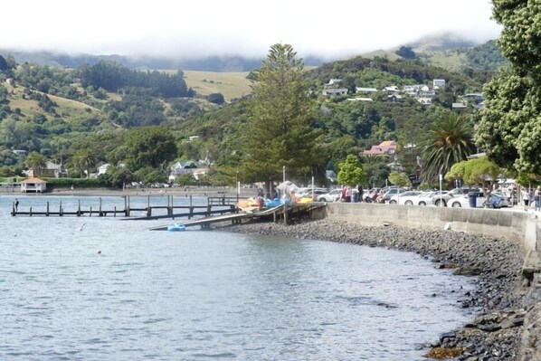 A coastal scene with a pier extending into calm waters, surrounded by lush greenery and residential buildings in the background. - Akaroa Central apartment (Akaroa)