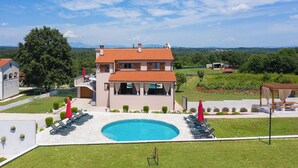 Ein zweigeschossiges Haus mit Swimmingpool, Sitzgelegenheiten im Freien und Blick ins Grüne.