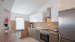 Eine moderne Küche mit Einbauofen, einem Edelstahlkühlschrank und einem Fenster mit durchsichtigen Vorhängen.