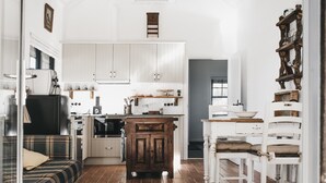 A compact kitchen with white cabinets, a wooden cabinet, a dining table with chairs, and a sofa. - Romantic luxury close to town, fine food dining and wineries. EV charger. (Orange)