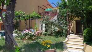 Un jardín con un sendero de piedra que lleva a una puerta, rodeado de follaje y plantas florecientes.