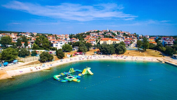 Vista aérea de un pueblo costero con playa, casas y cielo azul despejado.
