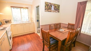 Un coin repas avec une table et des chaises en bois, un tableau au mur, et une cuisine avec des meubles blancs et un four à micro-ondes.