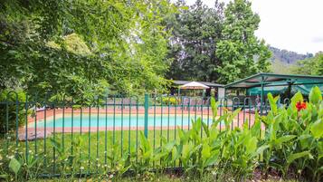 A swimming pool surrounded by lush greenery and a fenced area with outdoor seating.